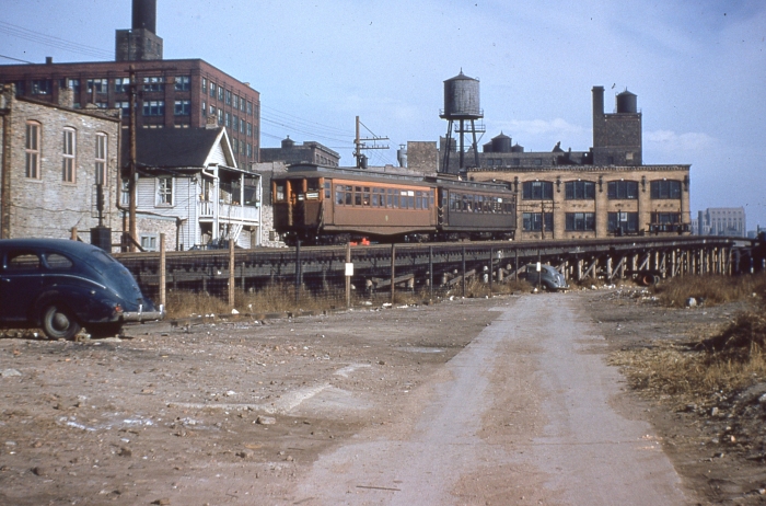 #12 - Two similar Met woods, one early with the fishbelly underframe, the later version with the straight frame, descend the east ramp from the Met "L" mainline, approaching the first grade crossing at Racine Avenue, probably early on in this operation, since Garfield Park was operated exclusively with wood cars. Answer: CTA 2815-2880 westbound, descending ramp to Van Buren near Racine on November 8, 1953. (Photo by Ray DeGroote)