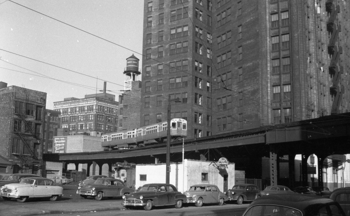 Frame 7 - "The Met "L" mainline at Clinton Street looking northwest with the Burlington building behind. A flat-door 6000 eastbound (Douglas?) with a single headlight above the end door. Wire suggests the west portal of the van Buren streetcar tunnel." -GF "About 321 S. Clinton." -DM Another clue is the sign for the Trav-Ler Radio Corp., which was located at 571 West Jackson Boulevard