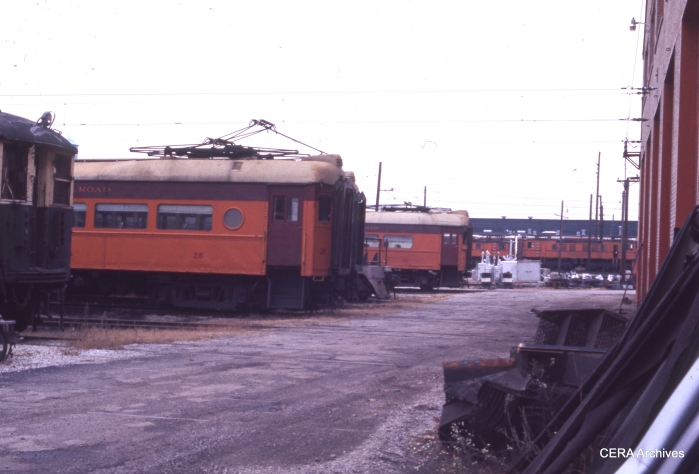South Shore cars 26 and 102 in Michigan City, October 1975. A CTA 4000-series "L" car is barely visible at left, on its way to a railway museum. (Photographer Unknown)